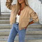 Femme portant un blouson beige tendance, t-shirt blanc et jean bleu, posant sur des escaliers en béton. Mode automne, style décontracté chic.