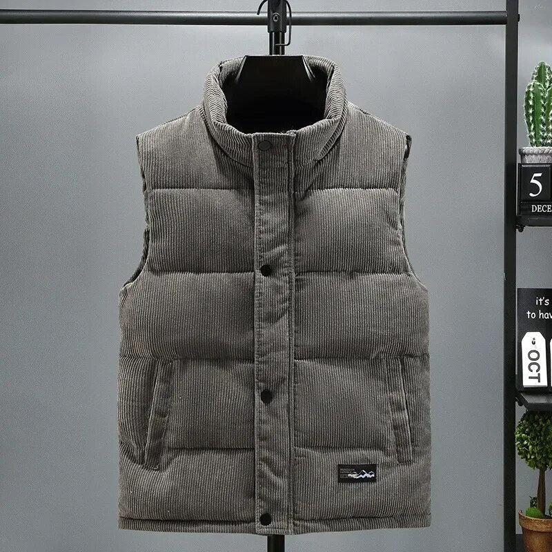 Gilet matelassé gris sans manches suspendu, col montant, boutons noirs, texture côtelée, style décontracté, mode automne-hiver, fond gris.