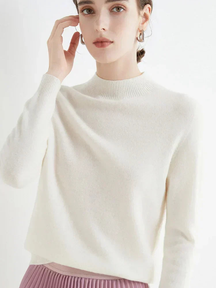 Femme portant un pull blanc en cachemire, manches longues, col rond, avec une jupe plissée rose. Mode élégante et minimaliste.