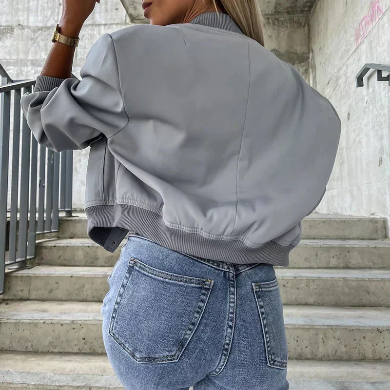 Femme portant un blouson gris tendance et un jean bleu, posant sur des escaliers en béton. Mode urbaine, style décontracté, look moderne.