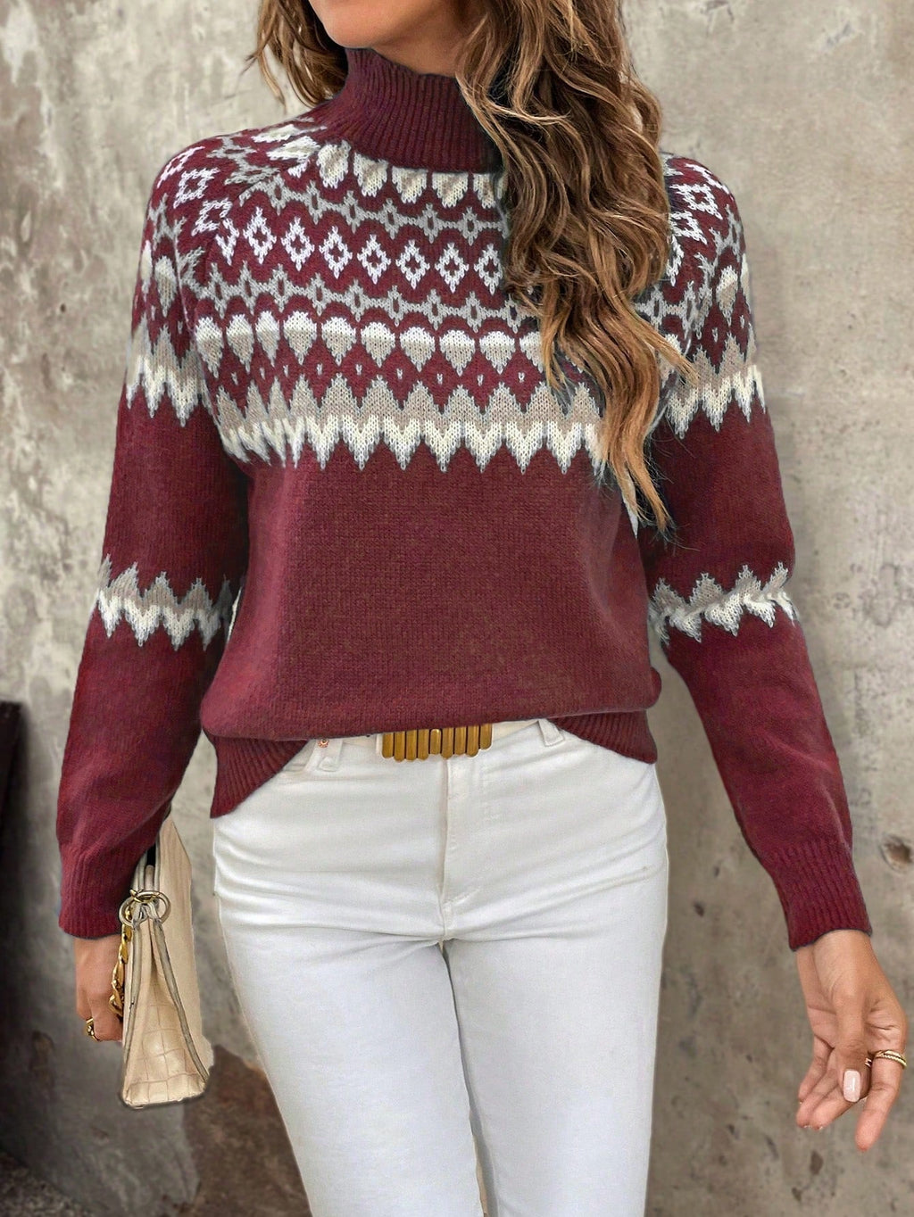 Femme portant un pull rouge à motifs géométriques blancs, manches longues, col montant, avec un pantalon blanc et un sac beige. Mode automne-hiver.