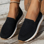 Chaussures mocassins noirs en maille pour femme, semelle blanche et marron, portées sur un sol en bois. Mode décontractée, confort, style estival.