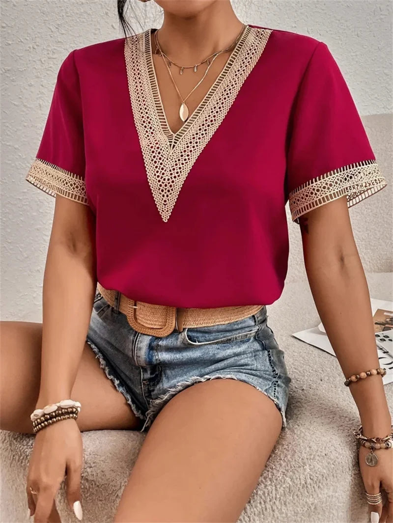 Femme portant un t-shirt rouge à col en V avec dentelle, short en jean, ceinture beige, colliers et bracelets. Mode estivale décontractée.
