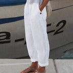 Pantalon blanc en lin pour femme, style décontracté, avec poches, porté avec des sandales marron, idéal pour l'été et les vacances en bord de mer.