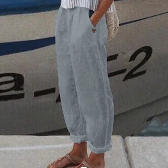 Personne portant un pantalon ample gris, debout près d'un bateau. Mode décontractée, style estival, bord de mer.