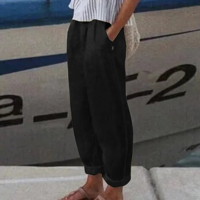 Personne portant un pantalon noir ample et une chemise rayée blanche, debout près d'un bateau. Mode décontractée, style estival, bord de mer.