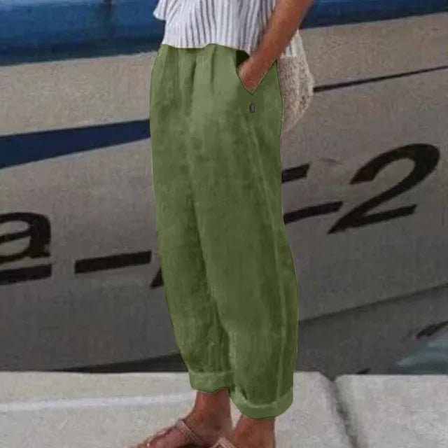 Personne portant un pantalon vert ample en lin, debout près d'un bateau. Mode décontractée estivale, style nautique, confort et élégance.