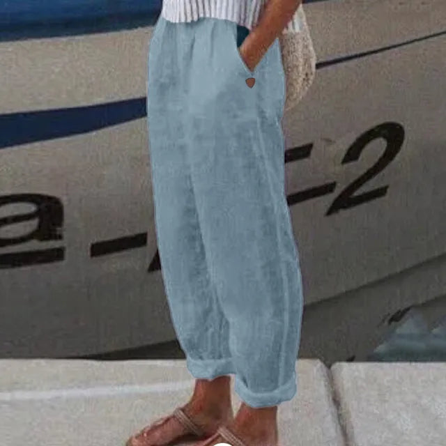 Pantalon ample en lin bleu clair, style décontracté, avec poches, porté par une personne debout près d'un bateau. Mode estivale confortable.