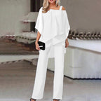 Femme en ensemble blanc élégant, blouse asymétrique et pantalon large, tenant une pochette noire. Mode chic, tenue de soirée moderne.