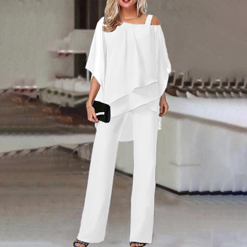 Femme en ensemble blanc élégant, blouse asymétrique et pantalon large, tenant une pochette noire. Mode chic, tenue de soirée moderne.