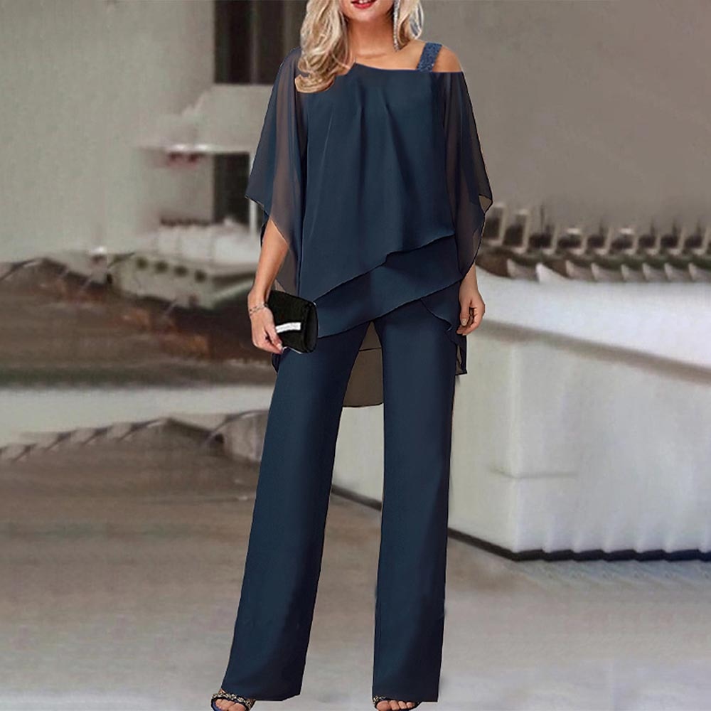 Femme en ensemble pantalon bleu marine élégant, blouse fluide, accessoires noirs, dans un intérieur moderne. Mode chic, tenue soirée, style sophistiqué.