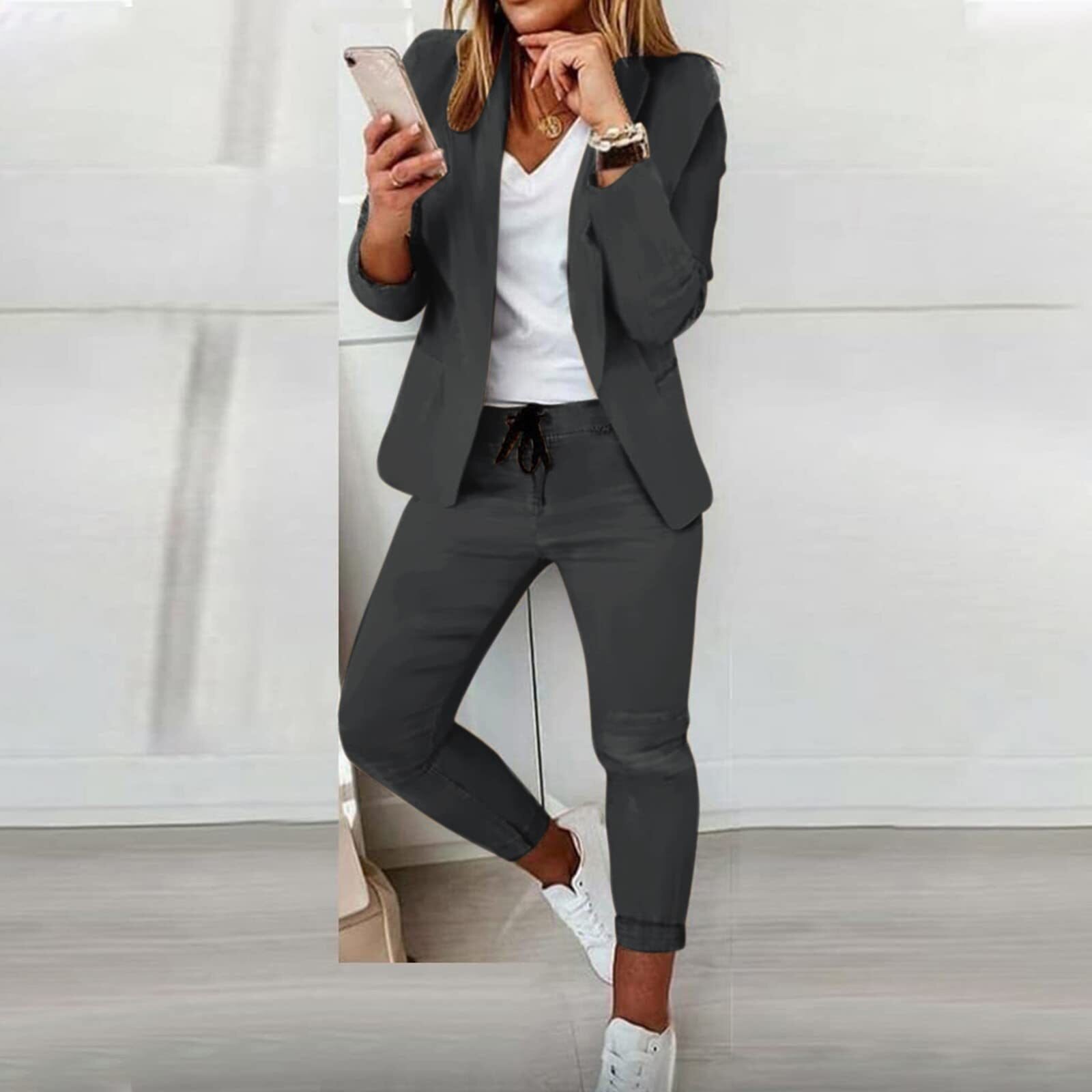 Femme en costume gris moderne, tenant un smartphone, portant des baskets blanches. Style décontracté chic, mode féminine contemporaine.