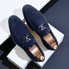 Mocassins en daim bleu marine élégants avec boucle métallique argentée, posés sur une surface blanche. Chaussures homme mode, style chic et moderne.
