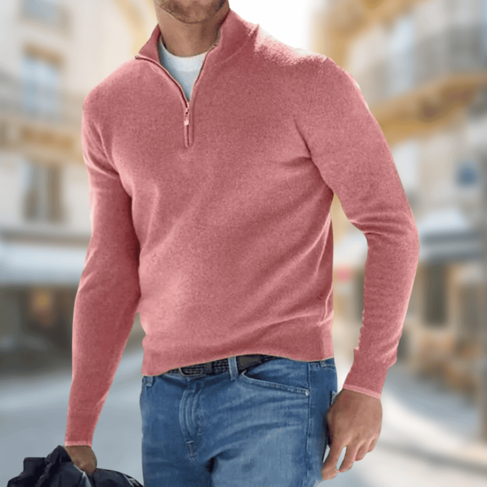 Homme portant un pull rose à col zippé, tenant un sac noir, debout dans une rue floue. Mode masculine, style décontracté, vêtements tendance.