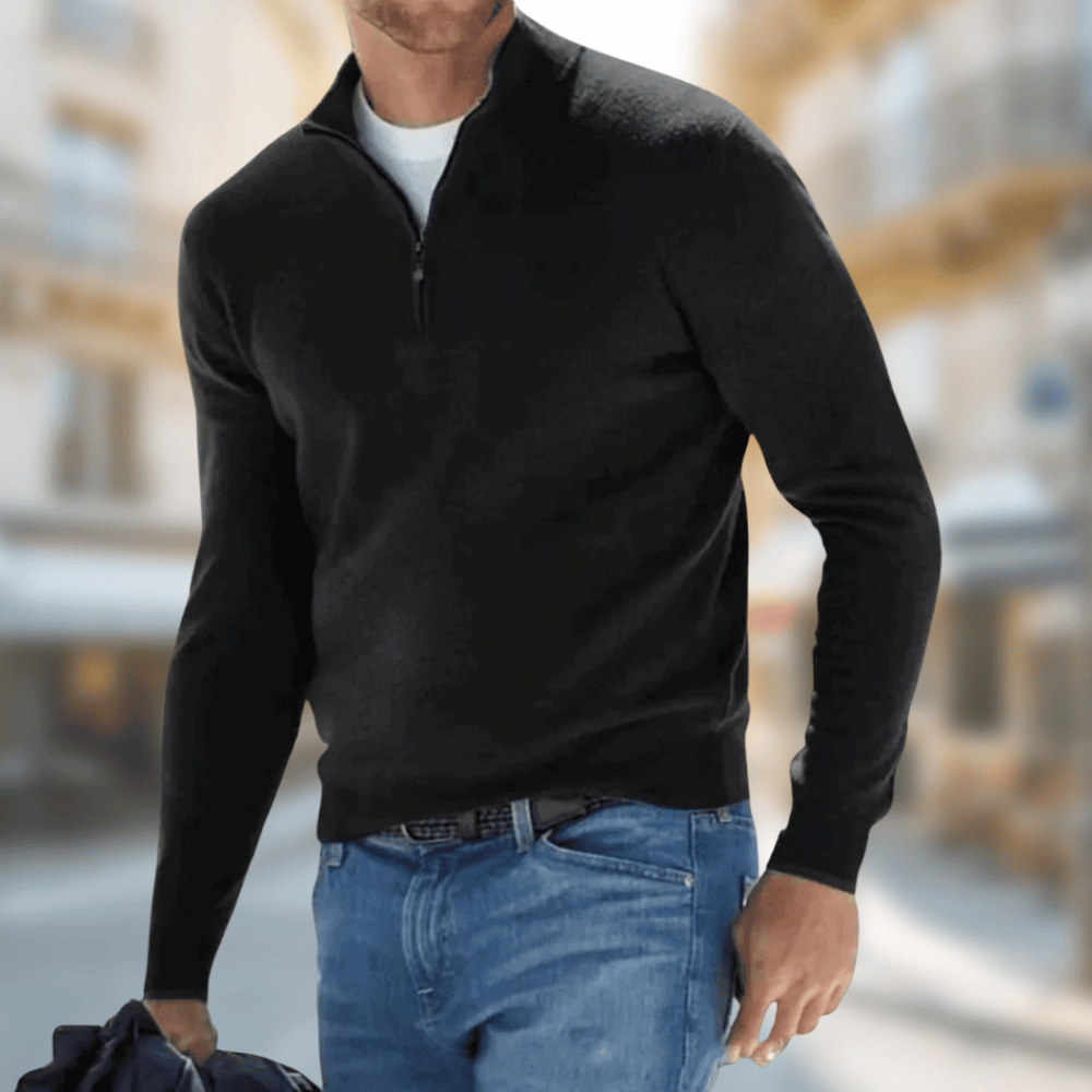 Homme portant un pull noir à col zippé et un jean bleu, marchant en ville. Mode masculine élégante, tenue décontractée chic, style urbain.