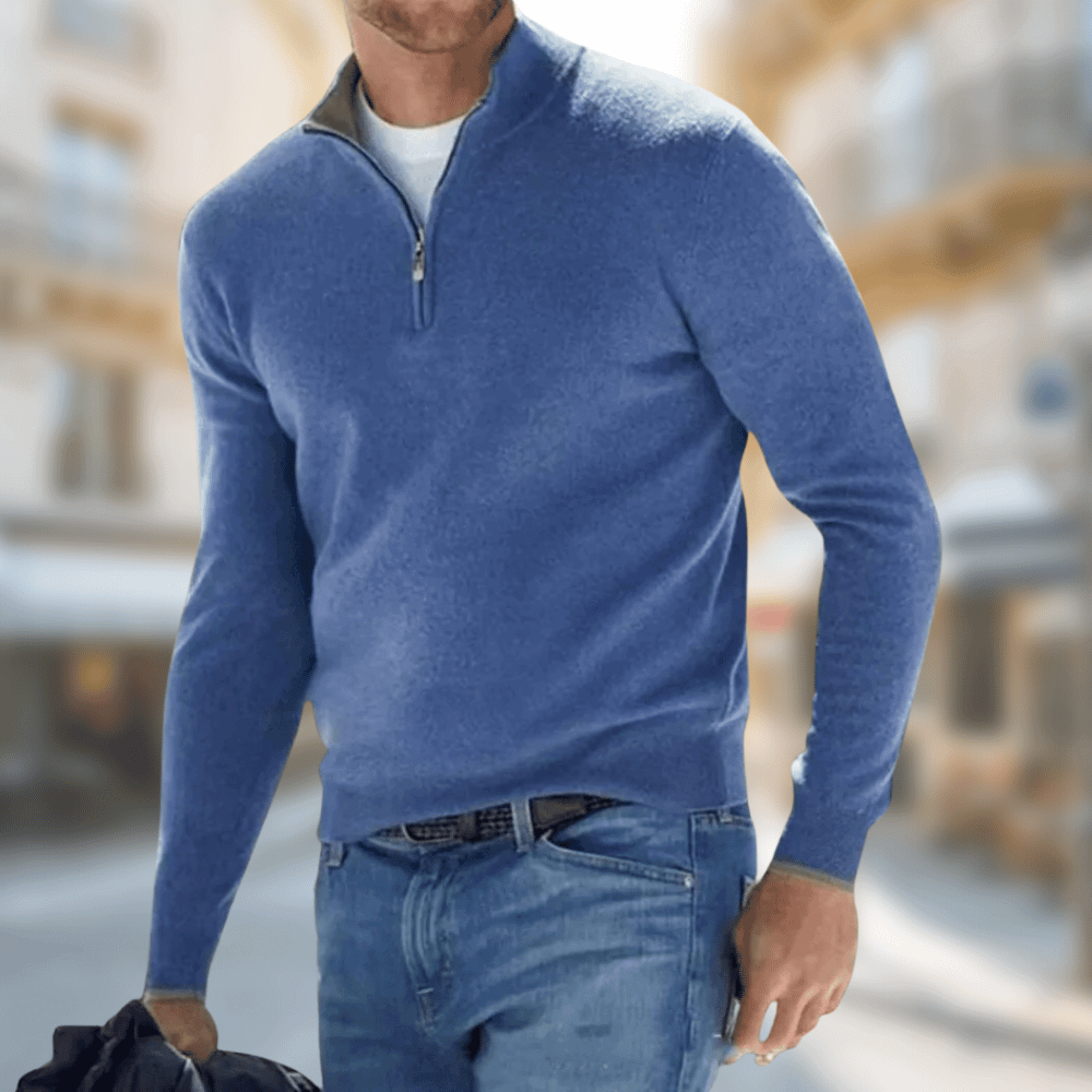 Homme portant un pull bleu à col zippé et un jean, marchant en ville. Mode masculine, tenue décontractée, style urbain élégant.