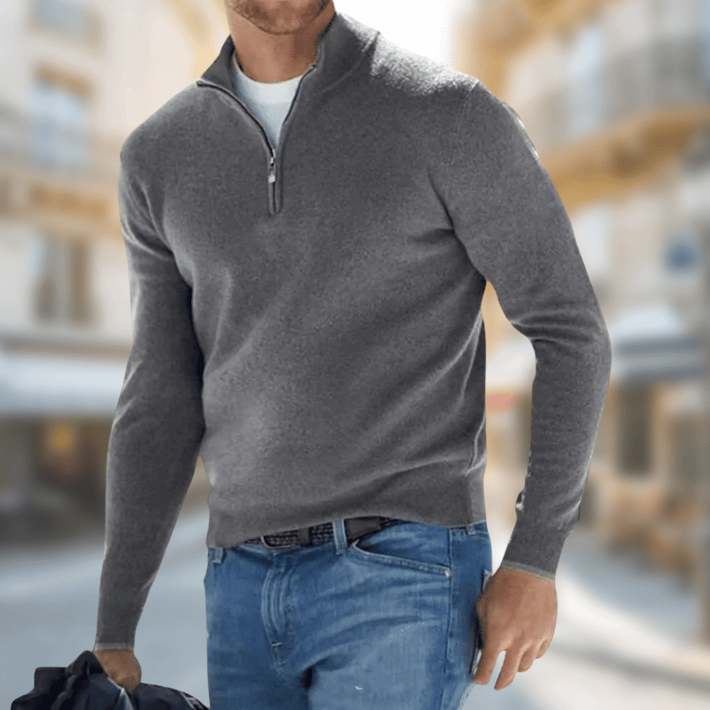 Homme portant un pull gris à col zippé et un jean bleu, marchant en ville. Mode masculine élégante, tenue décontractée automne-hiver.