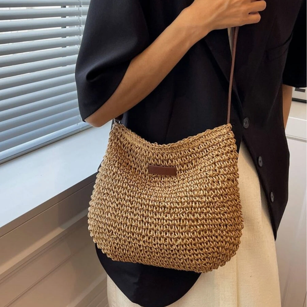 Sac en paille tressée porté à l'épaule par une personne en chemise noire. Accessoire de mode estival, tendance et élégant.