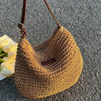 Sac à main en paille tressée avec anse en cuir marron, posé sur sol gris, accompagné de tulipes blanches. Mode, accessoires, tendance été.