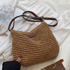 Sac à main en paille tressée marron avec bandoulière en cuir, posé sur une robe blanche. Accessoire mode tendance, idéal pour l'été.
