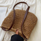 Sac en paille tressée avec bandoulière en cuir marron, posé sur un tissu blanc. Accessoire de mode estival, tendance et élégant.