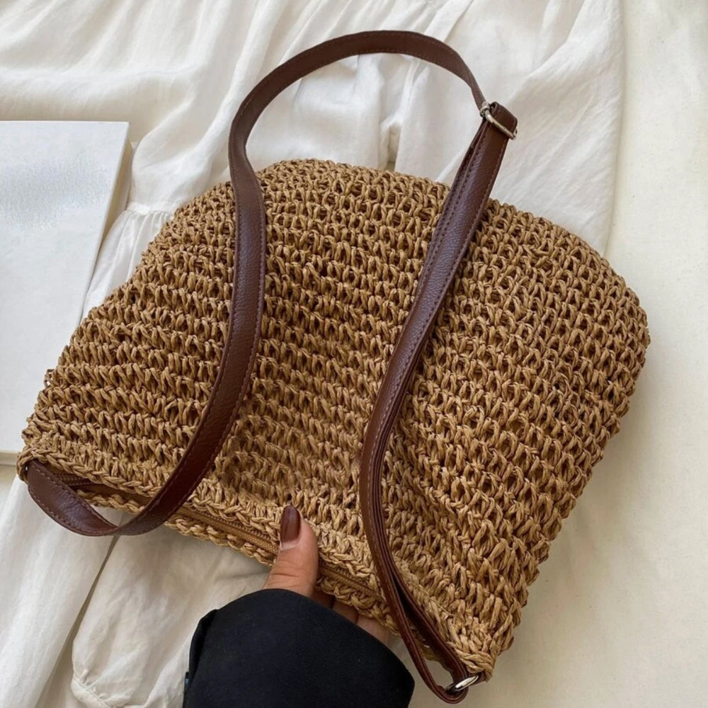 Sac en paille tressée avec bandoulière en cuir marron, posé sur un tissu blanc. Accessoire de mode estival, tendance et élégant.