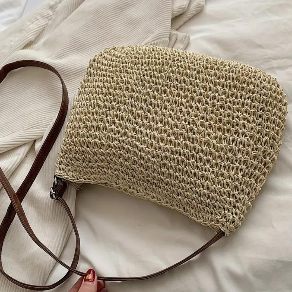 Sac à main en paille tressée avec bandoulière en cuir marron, posé sur un tissu blanc. Accessoire mode estival, tendance et naturel.