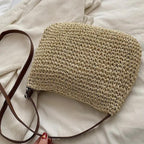 Sac à main en paille tressée avec bandoulière en cuir marron, posé sur un tissu blanc. Accessoire mode estival, tendance et naturel.