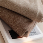 Deux couvertures en laine beige à motifs chevrons, empilées sur un livre, créant une ambiance chaleureuse et élégante pour la décoration intérieure.