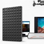 Disque dur externe noir texturé, ordinateur portable affichant une voiture rouge, cadre photo numérique avec plage, drone noir volant en arrière-plan.