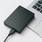 Disque dur externe noir connecté à un ordinateur portable argenté, câble USB branché, sur fond blanc. Stockage de données, technologie portable.
