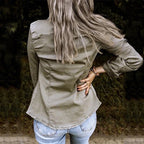 Femme de dos portant une chemise kaki et un jean bleu, cheveux longs et gris, posant en extérieur. Mode décontractée, style automne.