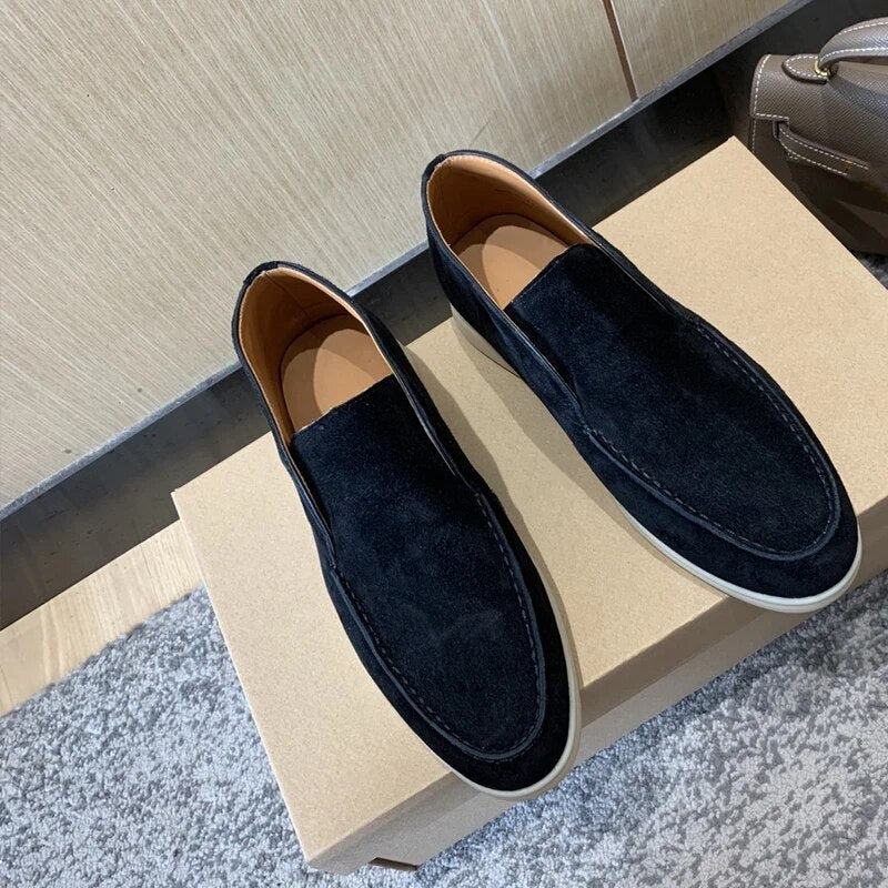 Chaussures mocassins en daim noir pour homme sur boîte en carton, posées sur tapis gris. Élégantes et modernes, idéales pour un style décontracté.