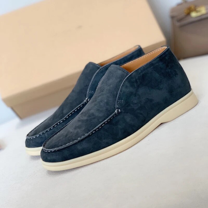 Chaussures mocassins en daim bleu marine pour homme, semelle blanche, posées sur une surface beige avec boîte en arrière-plan. Mode masculine élégante.