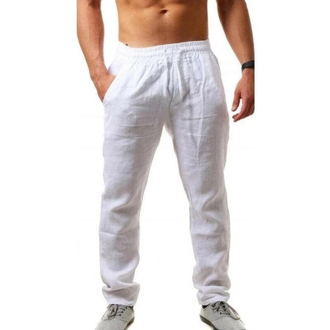 Homme portant un pantalon en lin blanc, taille élastique, mains dans les poches, torse nu, chaussures de sport grises. Mode décontractée masculine.