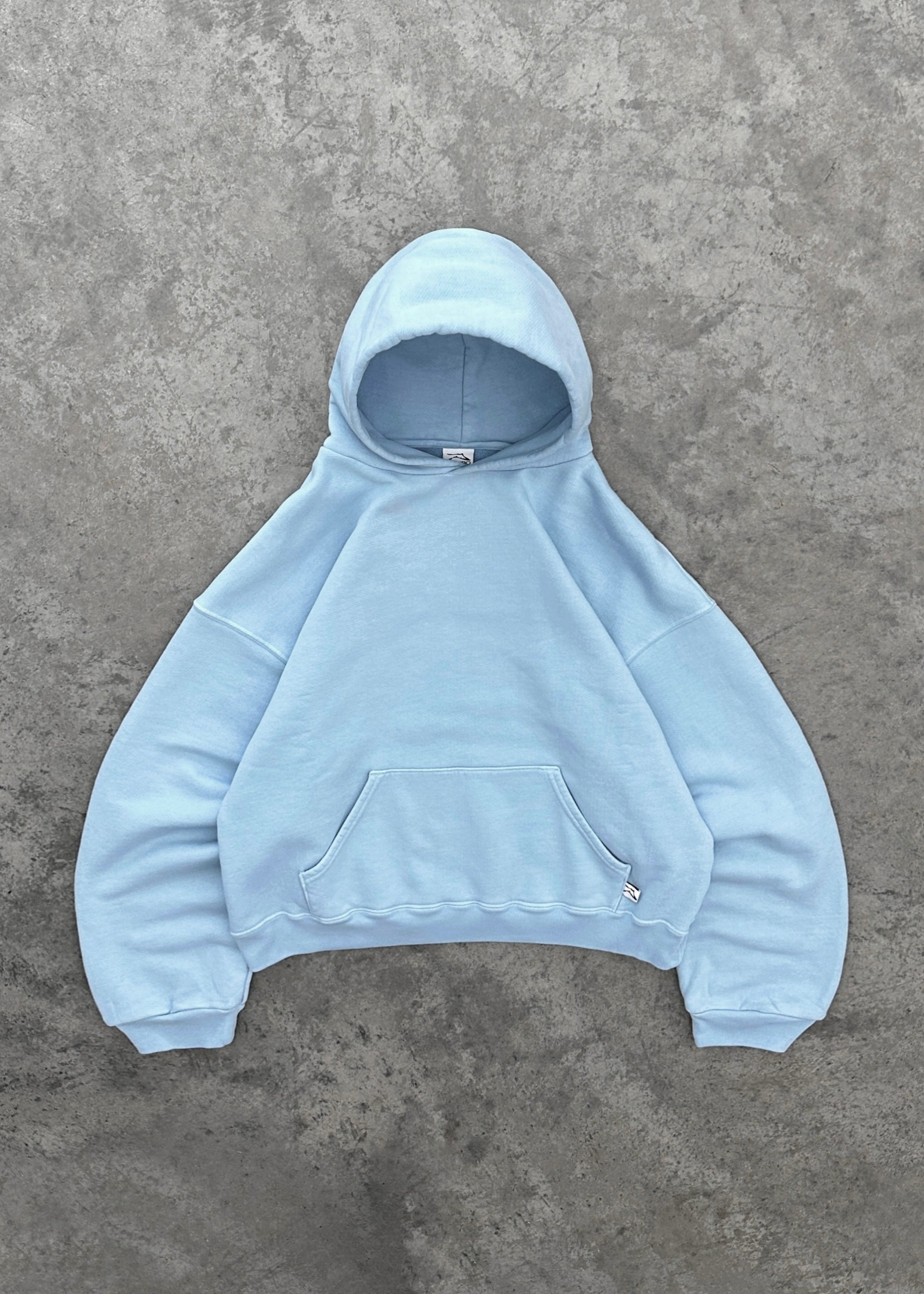 Sweat à capuche bleu clair sur fond gris, style décontracté, poche kangourou, manches longues, mode urbaine, vêtement confortable et tendance.