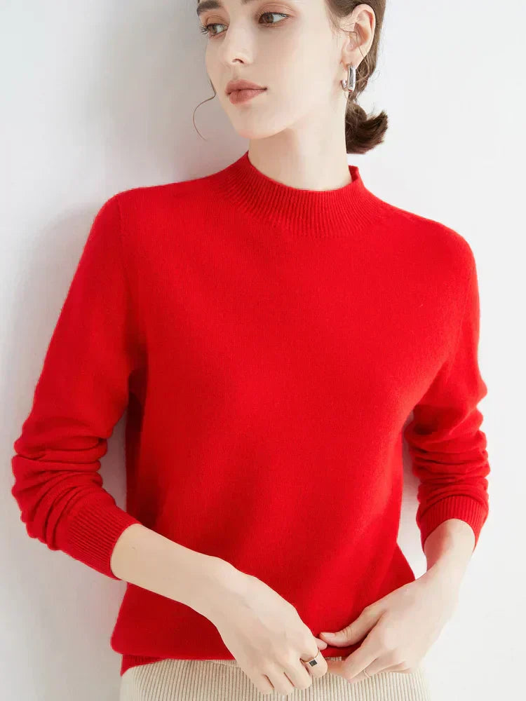 Femme portant un pull rouge en laine, manches longues, col rond, posant contre un mur blanc. Mode automne-hiver, style élégant et minimaliste.