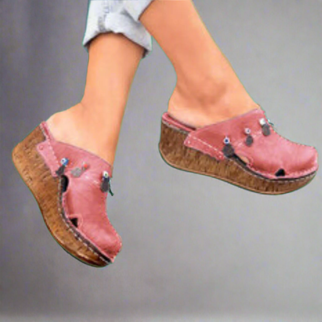 Sabots compensés roses en cuir avec semelle en bois, ornés de clous métalliques, portés par une personne en jean. Chaussures tendance et confortables.