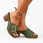 Sandales vertes à talons en bois avec boucle dorée, portées avec un bracelet de cheville en perles colorées. Mode estivale élégante et tendance.