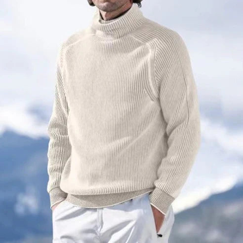 Homme portant un pull col roulé beige en laine, style décontracté, avec un fond de montagnes floues. Mode hiver, vêtements chauds pour homme.