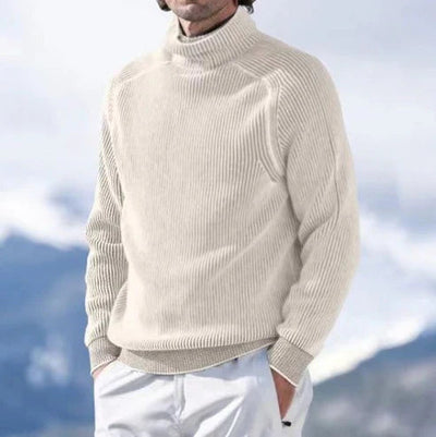 Homme portant un pull col roulé beige en laine, style décontracté, avec un fond de montagnes floues. Mode hiver, vêtements chauds pour homme.