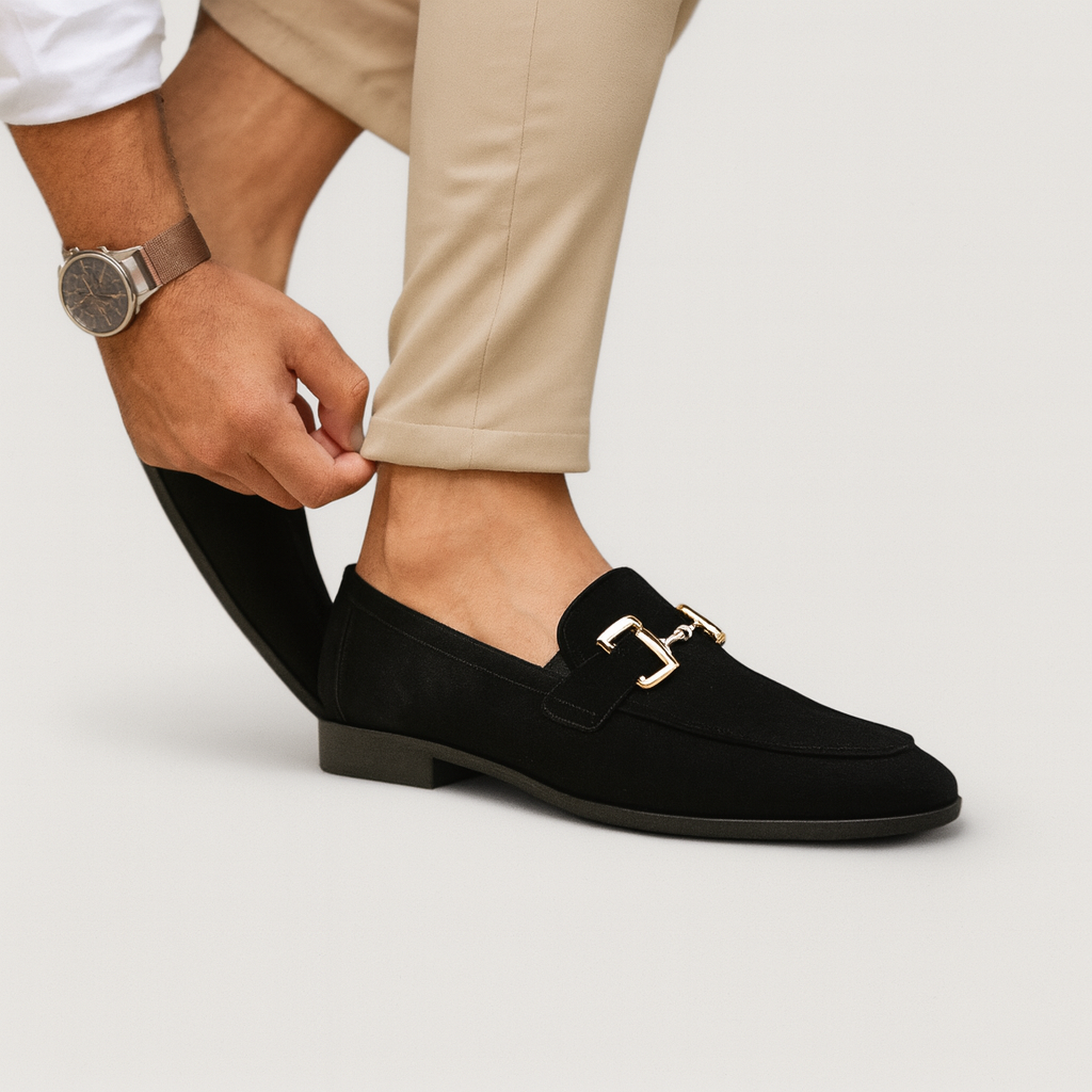 Homme ajustant son pantalon beige, portant des mocassins noirs élégants avec boucle dorée, montre-bracelet en cuir marron visible.