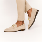 Chaussures mocassins beige en daim avec boucle dorée, portées avec un pantalon beige. Style élégant et moderne pour homme.