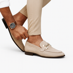 Homme ajustant des mocassins beige élégants avec boucle dorée, portant une montre-bracelet classique, pantalon beige. Mode masculine chic.