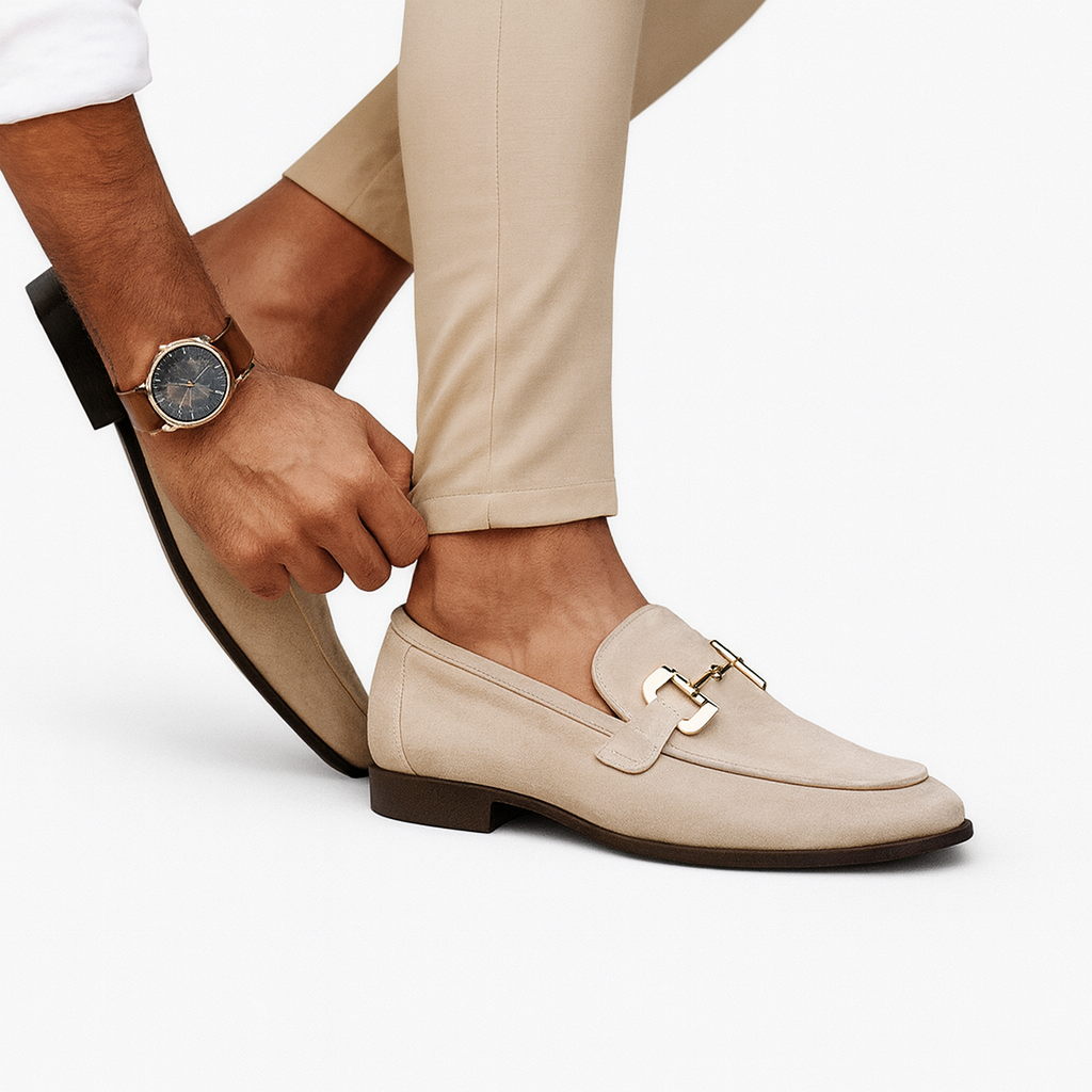 Homme ajustant des mocassins beige élégants avec boucle dorée, portant une montre-bracelet classique, pantalon beige. Mode masculine chic.