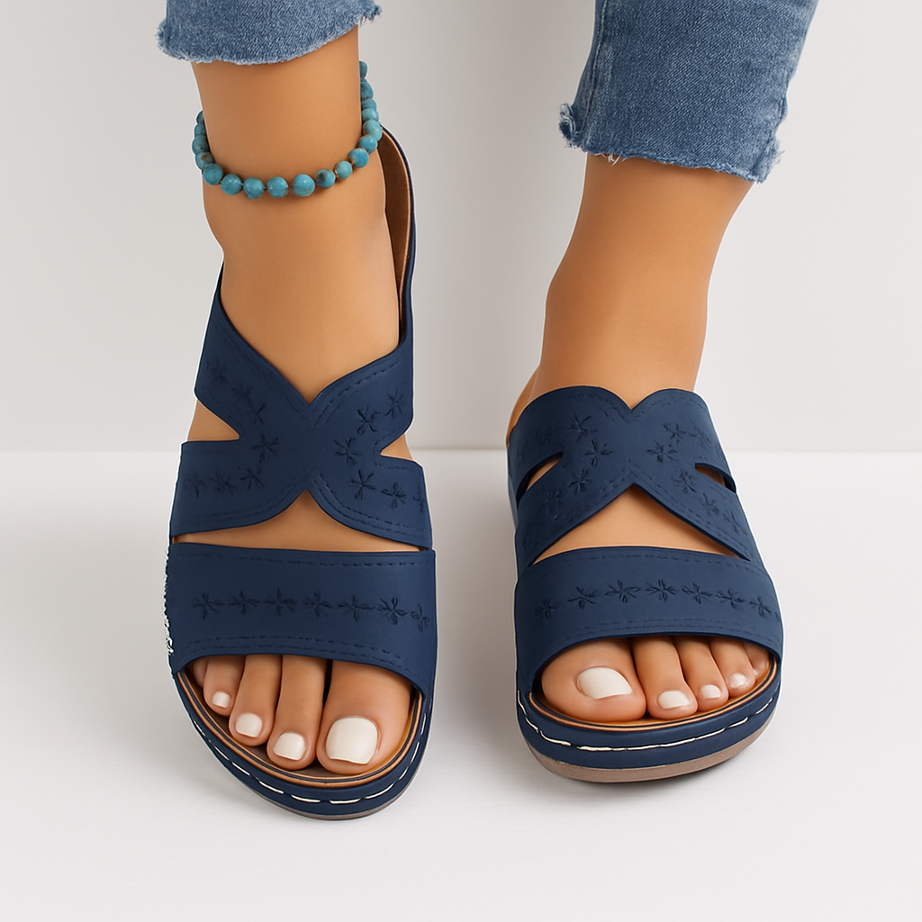 Sandales bleues en cuir avec motifs floraux portées par une femme, accompagnées d'un bracelet de cheville turquoise, sur fond blanc.