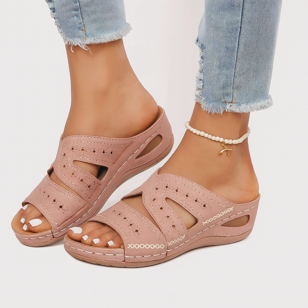 Sandales roses confortables pour femmes, avec talon compensé et détails ajourés, portées avec un jean déchiré et un bracelet de cheville perlé.