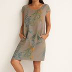 Robe d'été femme à manches courtes, motif floral vert et orange, poches latérales, style décontracté, fond beige. Mode féminine tendance.