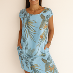 Robe d'été bleue à motifs floraux tropicaux, manches courtes, portée par une femme souriante. Mode féminine, tenue estivale élégante.