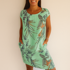 Robe verte à motifs floraux tropicaux, manches courtes, portée par une femme souriante. Mode estivale, tenue décontractée, style tropical.